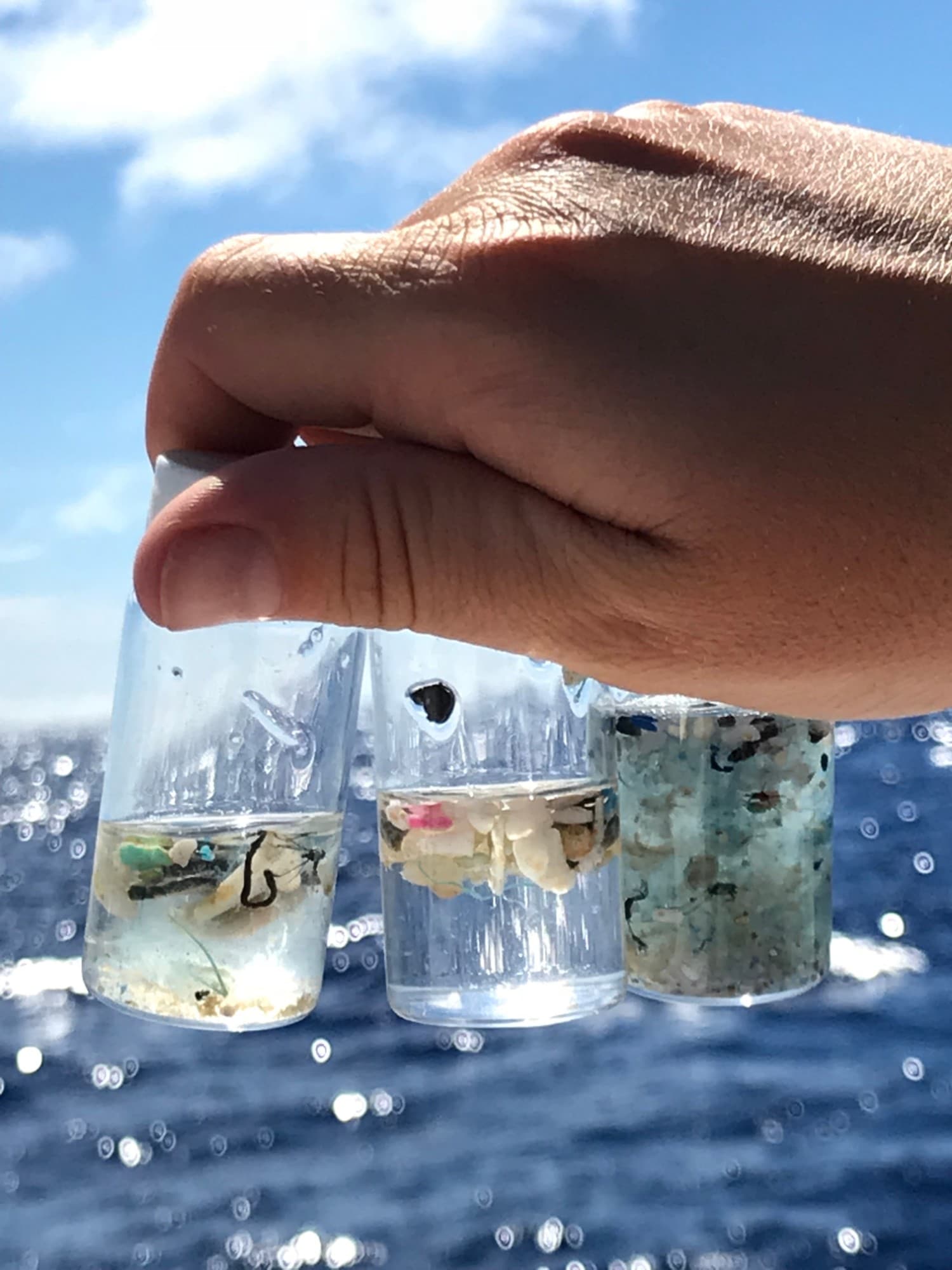 Sample vials of collected microplastics held up against the sea